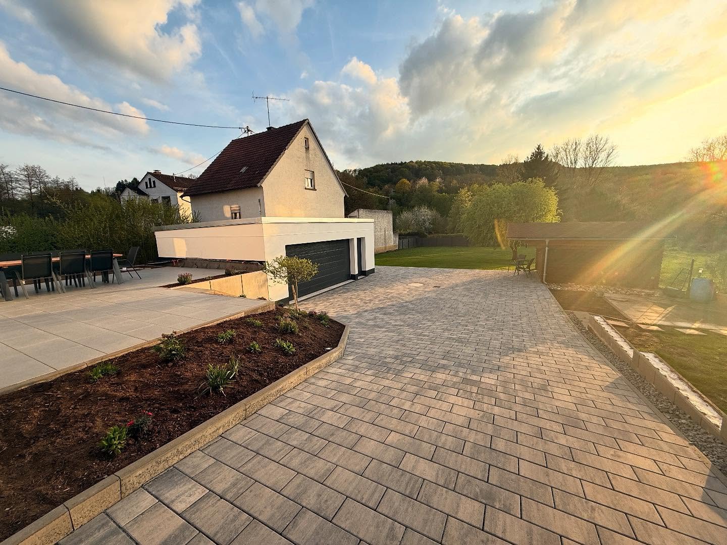 Fertiges Grundstück in der Abendsonne: gepflasterter Hof, Plattenterrasse und gemauerte Doppelgarage
